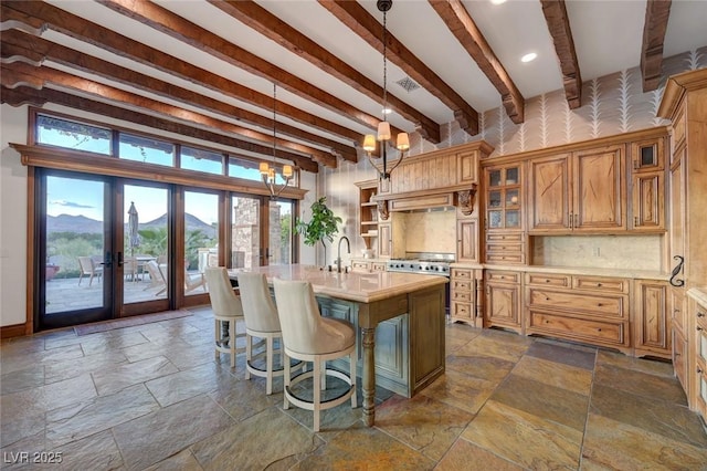15 Rue Du Rivoli Pl, Henderson, NV 89011 - kitchen featuring stone tile floors, light countertops, beam ceiling, an island with sink, and french doors