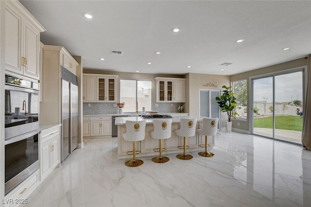 10550 Patrington Ct, Las Vegas, NV 89183 - kitchen featuring marble finish floor, backsplash, visible vents, glass insert cabinets, and appliances with stainless steel finishes