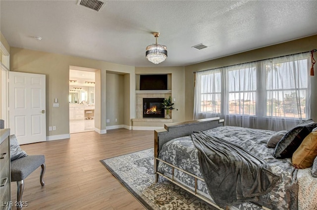 10550 Patrington Ct, Las Vegas, NV 89183 - bedroom with light wood-type flooring, an inviting chandelier, a tiled fireplace, baseboards, and visible vents