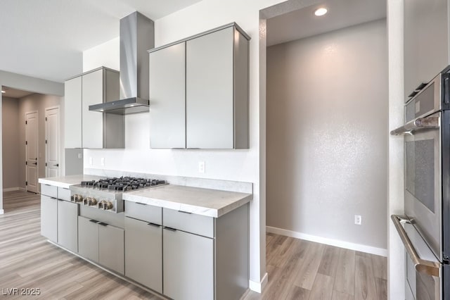 kitchen with light wood finished floors, gray cabinetry, baseboards, and appliances with stainless steel finishes