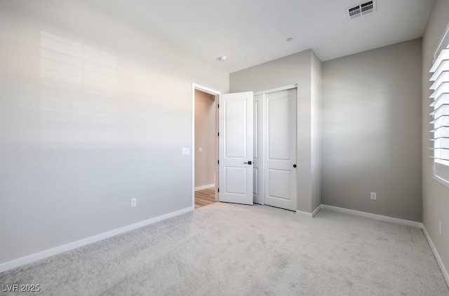 unfurnished bedroom featuring baseboards, light carpet, a closet, and visible vents