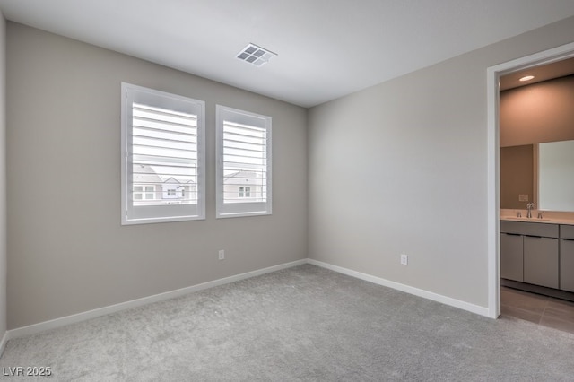 unfurnished bedroom featuring ensuite bathroom, light carpet, baseboards, and visible vents