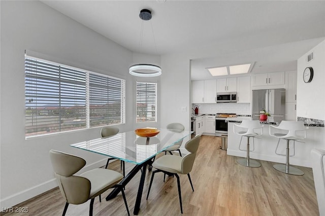 dining space featuring baseboards, visible vents, and light wood finished floors