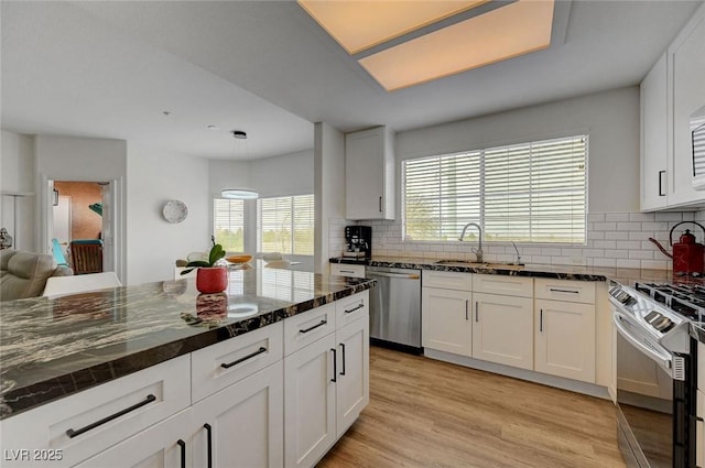 kitchen featuring white cabinetry, light wood-type flooring, dark stone counters, a sink, and appliances with stainless steel finishes