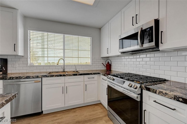 kitchen featuring a sink, light wood finished floors, white cabinetry, appliances with stainless steel finishes, and plenty of natural light