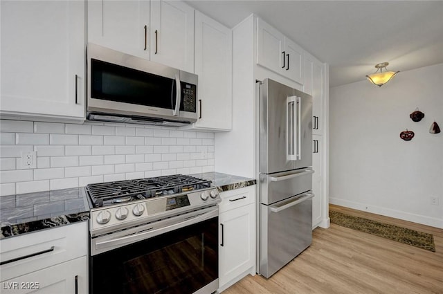kitchen with light wood finished floors, stainless steel appliances, tasteful backsplash, dark stone countertops, and white cabinetry