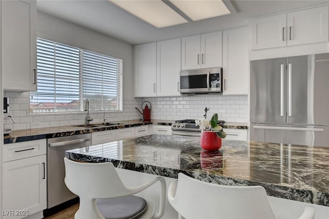 kitchen with a kitchen breakfast bar, tasteful backsplash, stainless steel appliances, a sink, and white cabinets