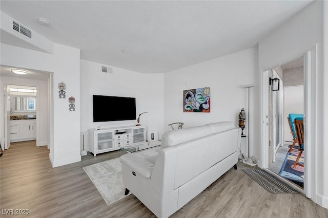 living room with baseboards, visible vents, and light wood-style flooring