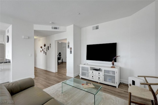 living area with baseboards, visible vents, and wood finished floors