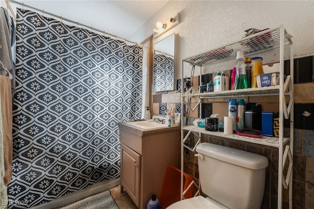 full bathroom with vanity, curtained shower, a textured wall, tile patterned floors, and toilet