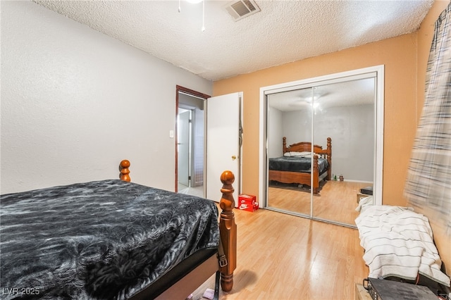 bedroom featuring ceiling fan, a textured ceiling, a closet, visible vents, and wood finished floors