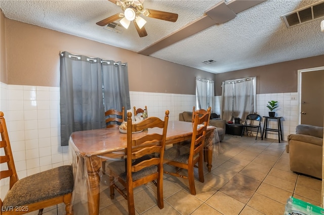 dining room featuring light tile patterned flooring, a ceiling fan, visible vents, and tile walls
