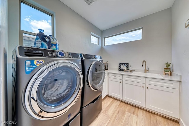laundry area featuring a sink, cabinet space, light wood finished floors, washing machine and dryer, and visible vents
