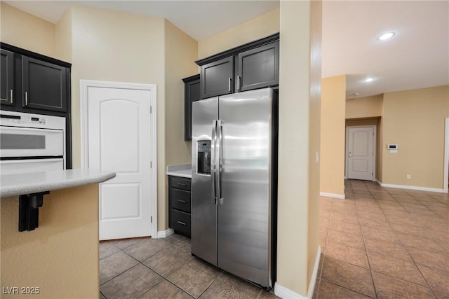 9173 Whitekirk Pl, Las Vegas, NV 89145 - kitchen with stainless steel refrigerator with ice dispenser, light countertops, tile patterned floors, baseboards, and dark cabinetry