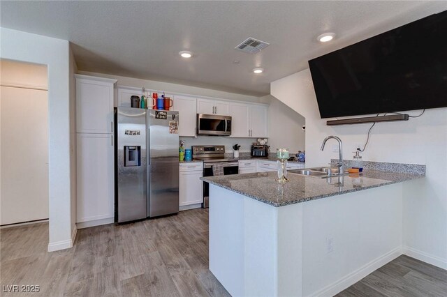 6804 Surf Green Ct, North Las Vegas, NV 89086 - kitchen featuring stainless steel appliances, a sink, light wood-style flooring, stone countertops, and a peninsula