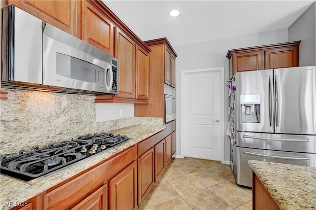 kitchen featuring light stone countertops, appliances with stainless steel finishes, brown cabinetry, and light tile patterned floors