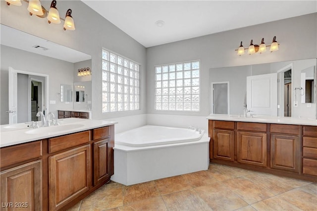 bathroom featuring visible vents, two vanities, a sink, and a bath