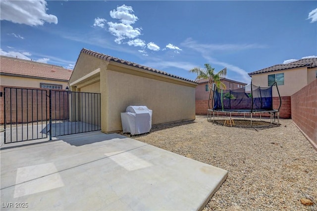view of side of home featuring fence, a trampoline, stucco siding, and a patio