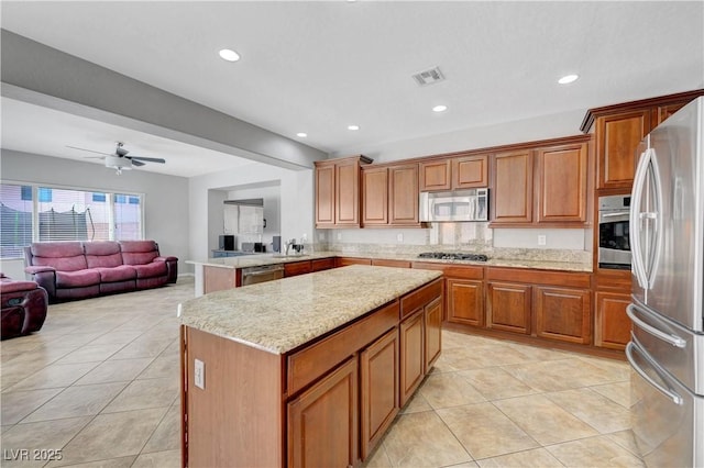 kitchen with brown cabinetry, visible vents, appliances with stainless steel finishes, light tile patterned floors, and open floor plan