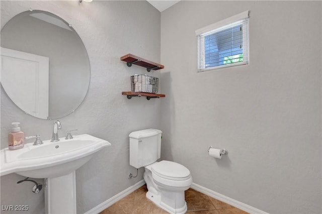 half bath with baseboards, tile patterned floors, and toilet