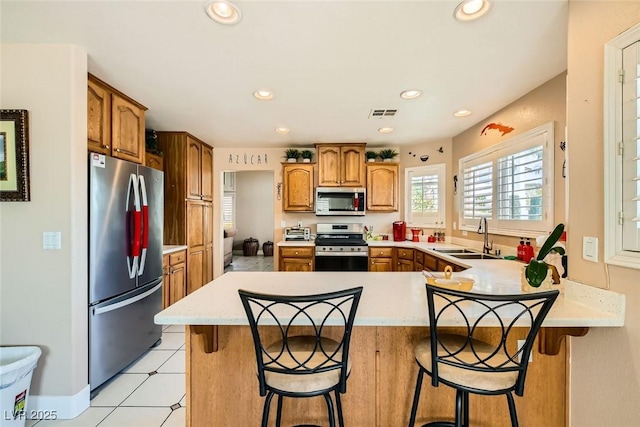 kitchen featuring recessed lighting, stainless steel appliances, a sink, a peninsula, and brown cabinetry