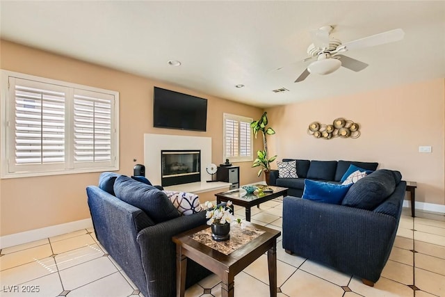 living area featuring visible vents, baseboards, ceiling fan, a glass covered fireplace, and light tile patterned floors