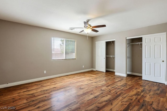 unfurnished bedroom with two closets, baseboards, visible vents, ceiling fan, and wood finished floors