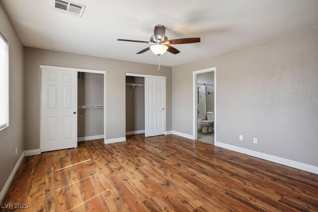 unfurnished bedroom with wood finished floors, ensuite bathroom, baseboards, visible vents, and two closets