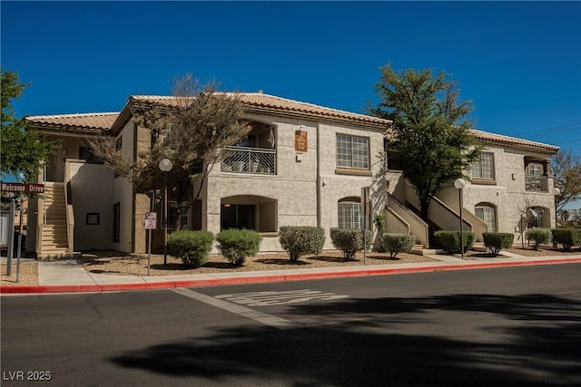 view of front facade featuring stucco siding, stairs, and a tiled roof