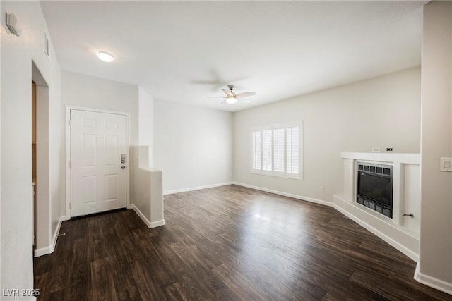 unfurnished living room with baseboards, dark wood-style floors, a glass covered fireplace, and ceiling fan