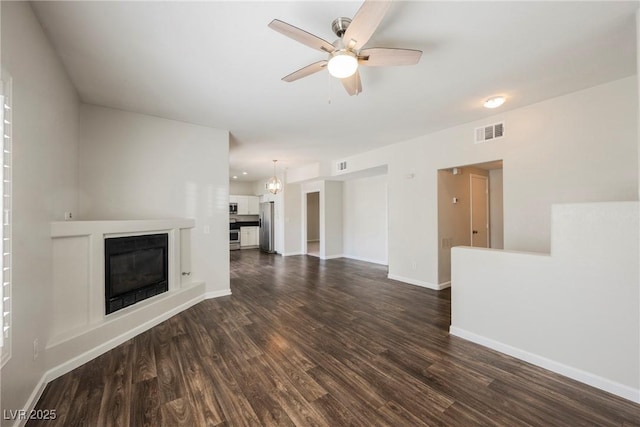 unfurnished living room with dark wood-style flooring, visible vents, baseboards, ceiling fan, and a glass covered fireplace
