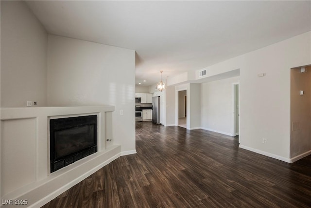 unfurnished living room with dark wood-type flooring, baseboards, a fireplace with raised hearth, and visible vents