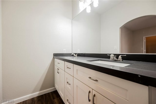 bathroom featuring baseboards, wood finished floors, double vanity, and a sink