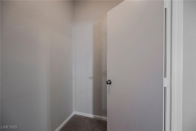 corridor with baseboards and dark colored carpet