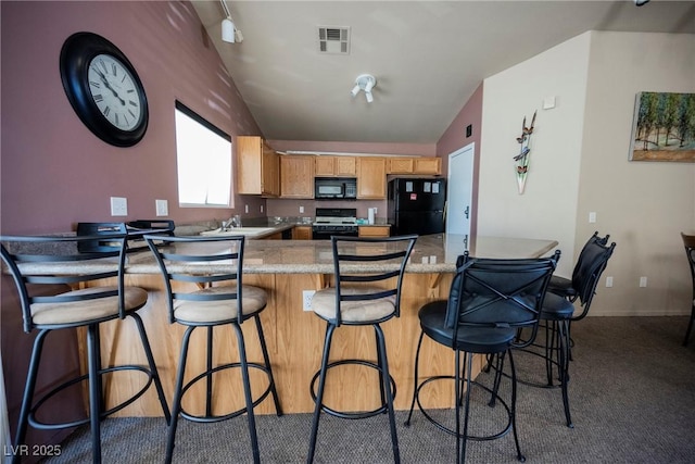 kitchen featuring light countertops, vaulted ceiling, visible vents, a peninsula, and black appliances