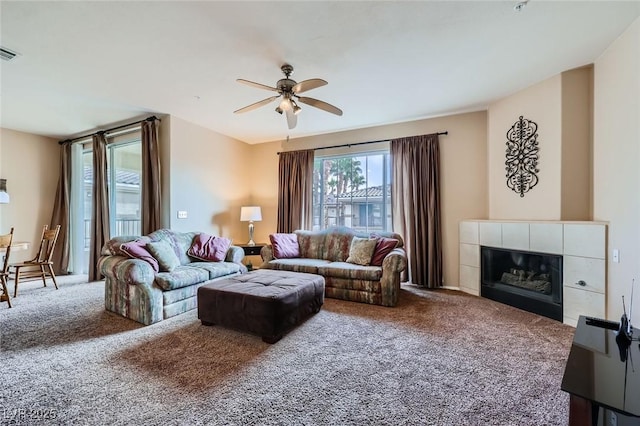 living area with a tiled fireplace, visible vents, a ceiling fan, and carpet flooring