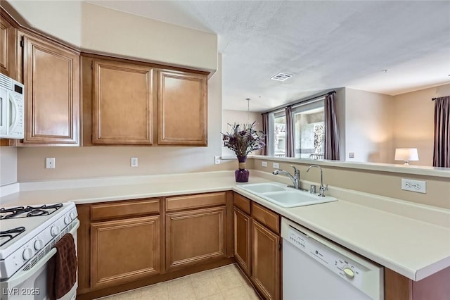 kitchen featuring brown cabinets, a sink, visible vents, a peninsula, and white appliances