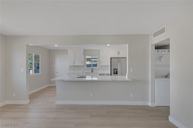 kitchen featuring white cabinetry, light countertops, stainless steel fridge with ice dispenser, stacked washer and dryer, and visible vents