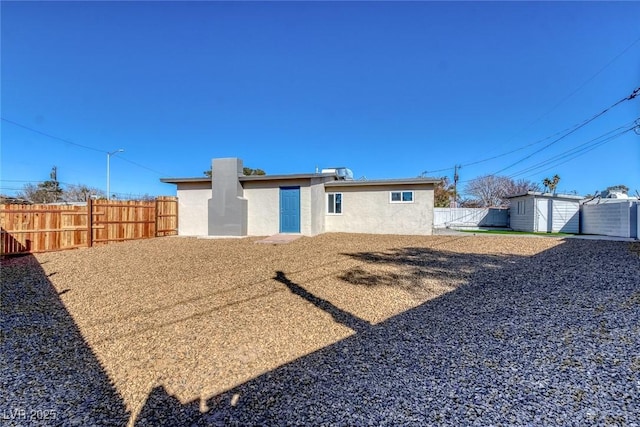 back of house featuring stucco siding, an outbuilding, fence, and a storage unit