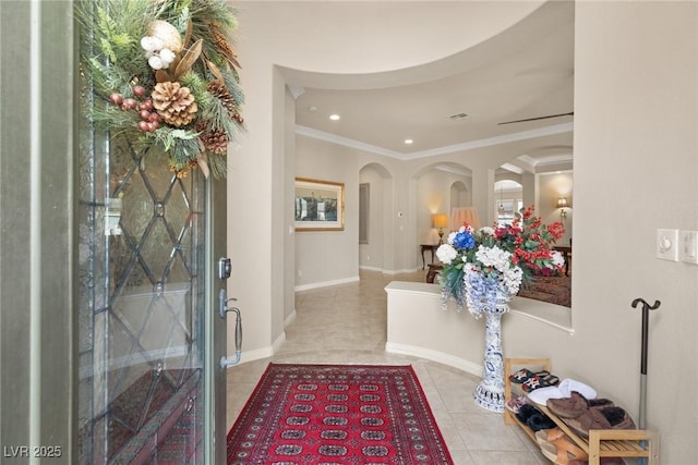 tiled foyer featuring ornamental molding, arched walkways, baseboards, and recessed lighting