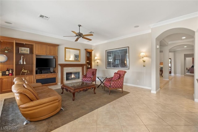 living area with a glass covered fireplace, light tile patterned floors, visible vents, arched walkways, and ceiling fan