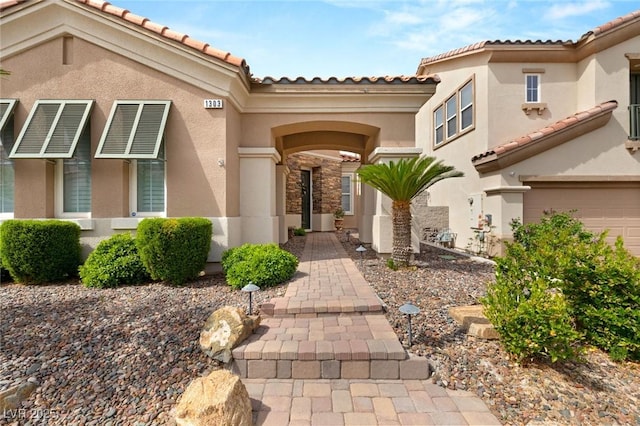 doorway to property with stucco siding, a tile roof, and a garage