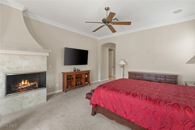 carpeted bedroom featuring a tiled fireplace, arched walkways, and crown molding