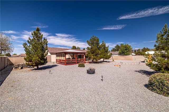 rear view of house with a gazebo, a deck, a fenced backyard, and a fire pit