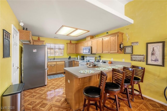 kitchen with a peninsula, a breakfast bar, appliances with stainless steel finishes, a sink, and light countertops