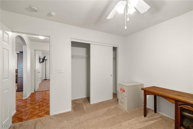 interior space with a closet, baseboards, light carpet, a ceiling fan, and arched walkways