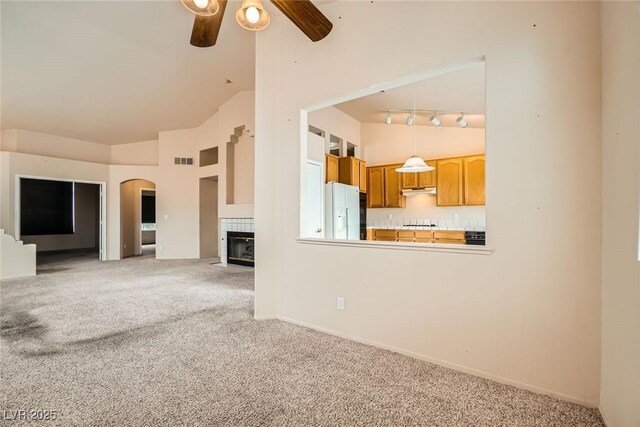 9532 Calico Garden Ave, Las Vegas, NV 89134 - unfurnished living room with carpet flooring, high vaulted ceiling, ceiling fan, a tiled fireplace, and track lighting