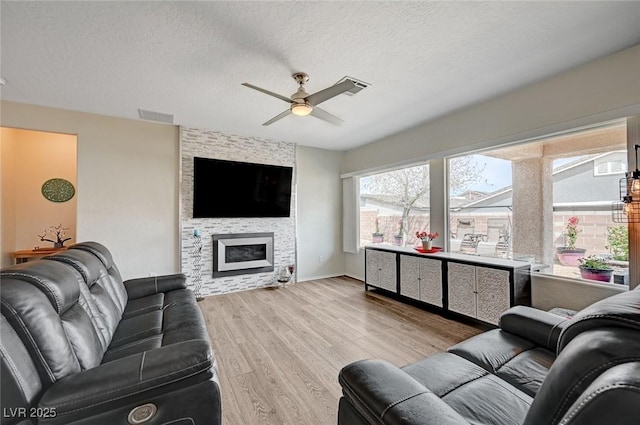 7460 Chaffinch St, North Las Vegas, NV 89084 - living room featuring ceiling fan, light wood-style flooring, a textured ceiling, and a large fireplace