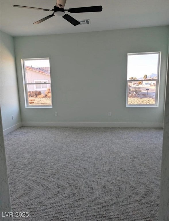 carpeted spare room with baseboards, visible vents, and a ceiling fan