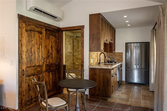 kitchen featuring stainless steel appliances, a sink, backsplash, a wall mounted air conditioner, and light stone counters